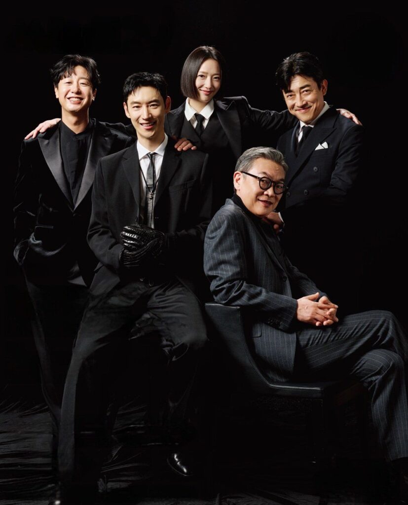 taxi driver 3 potret para anggota Rainbow Taxi dalam drama Korea Taxi Driver 3 yang tampil kompak mengenakan setelan hitam dengan latar belakang gelap.